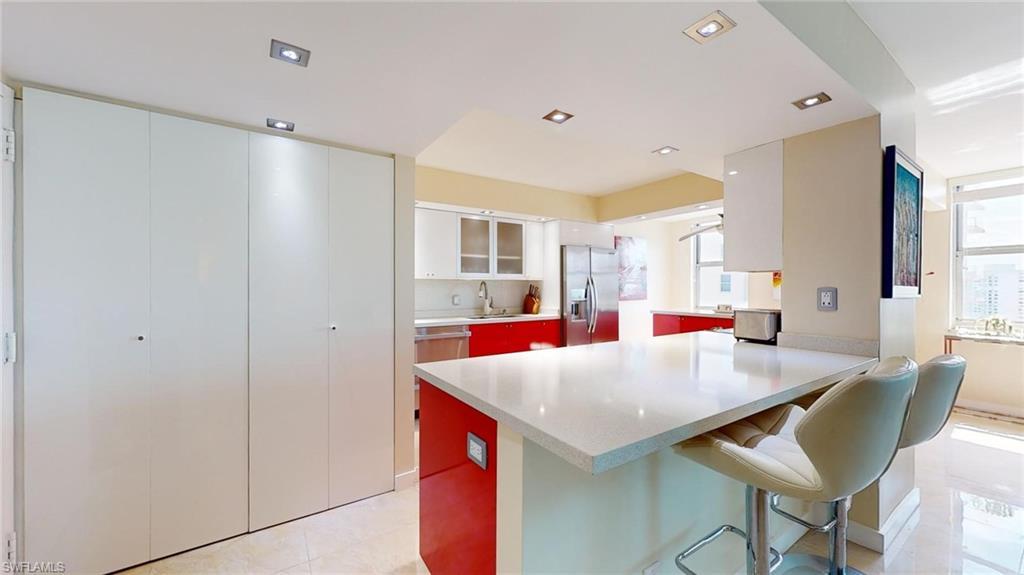 Image 3: Kitchen featuring glass insert cabinets, a kitchen bar, a peninsula, stainless steel fridge, and white cabinetry