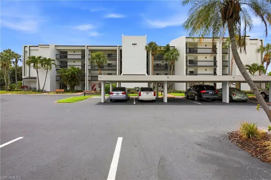 Image 1: Contemporary multi-story building featuring covered parking, multiple balconies with dark railings, a light-colored exterior, and surrounding tropical landscaping