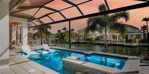 Image 3: Pool at dusk with a patio, a water view, a pool with connected hot tub, glass enclosure, and a sunroom