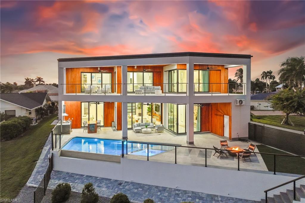 Image 4: Back of property at dusk with a balcony, a patio, an outdoor living space with a fire pit, an outdoor pool, and a fenced backyard