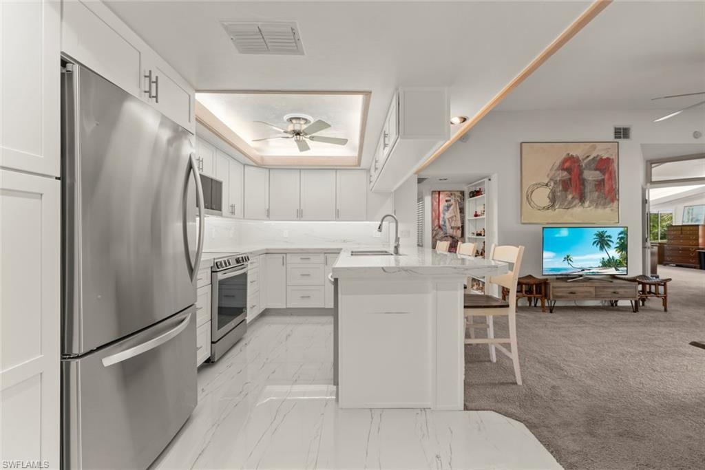 Image 4: Kitchen with ceiling fan, stainless steel appliances, light tile counters, white cabinets, and a breakfast bar area
