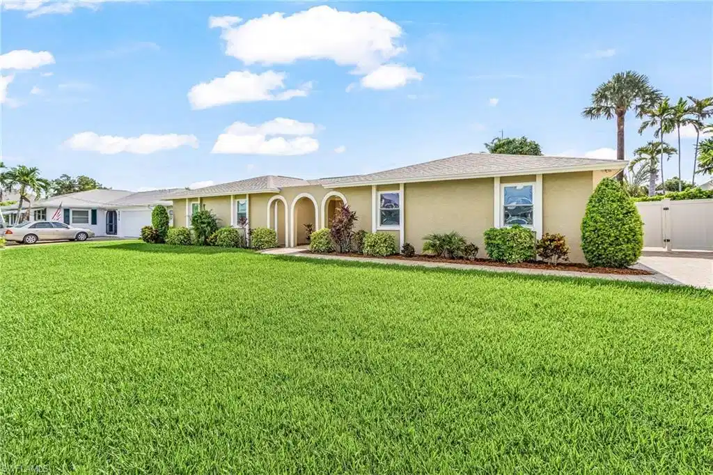 Image 1: Spacious front lawn with mature landscaping, stucco exterior, arched entryways, white-framed windows, and a privacy fence