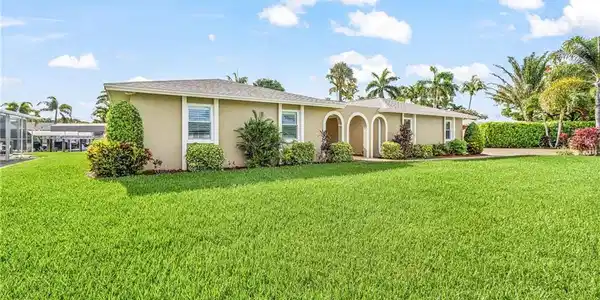 Image 3: Expansive green lawn with a single-story residence featuring a tan exterior, multiple windows, and an arched entry