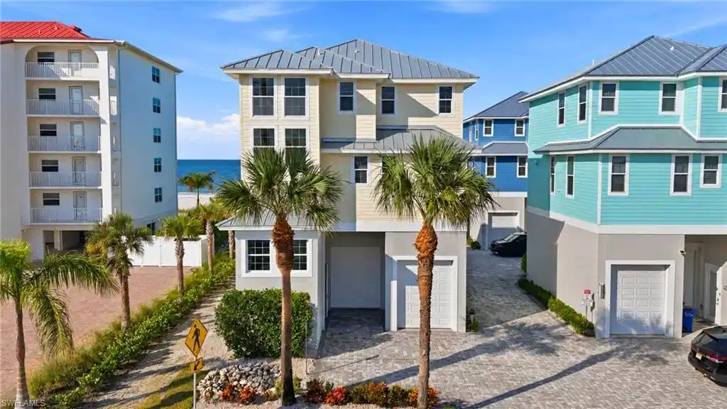 Image 1: Modern coastal residence featuring a striking cream and black exterior with metal roof accents, flanked by mature palm trees - Virtually Edited Image