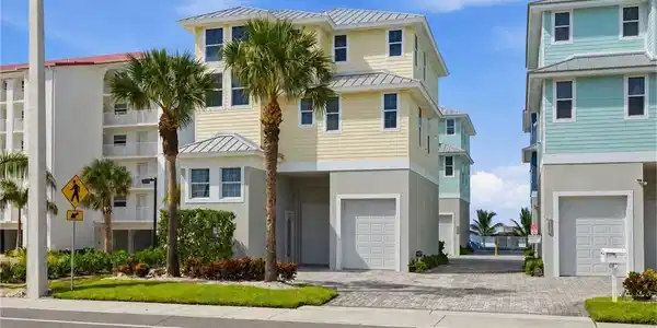 Image 3: Modern coastal residence featuring a striking cream and black exterior with metal roof accents, flanked by mature palm trees - Virtually Edited Image
