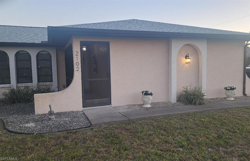 Image 1: Cream stucco exterior with a dark grey shingle roof