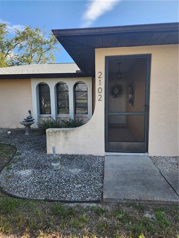 Image 2: Stucco exterior featuring arched windows with black frames, a screened entry door, and a gravel-covered front yard
