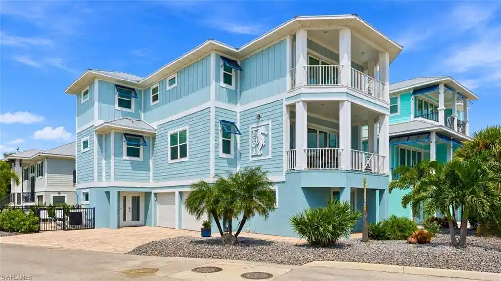 Image 1: Multi-story residence featuring light blue siding, white trim, a paver driveway, an integrated two-car garage, and established landscaping - Virtually Edited Image