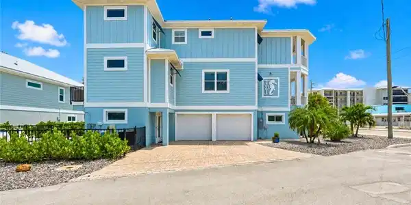 Image 3: Multi-story residence featuring light blue siding, white trim, a paver driveway, an integrated two-car garage, and established landscaping - Virtually Edited Image