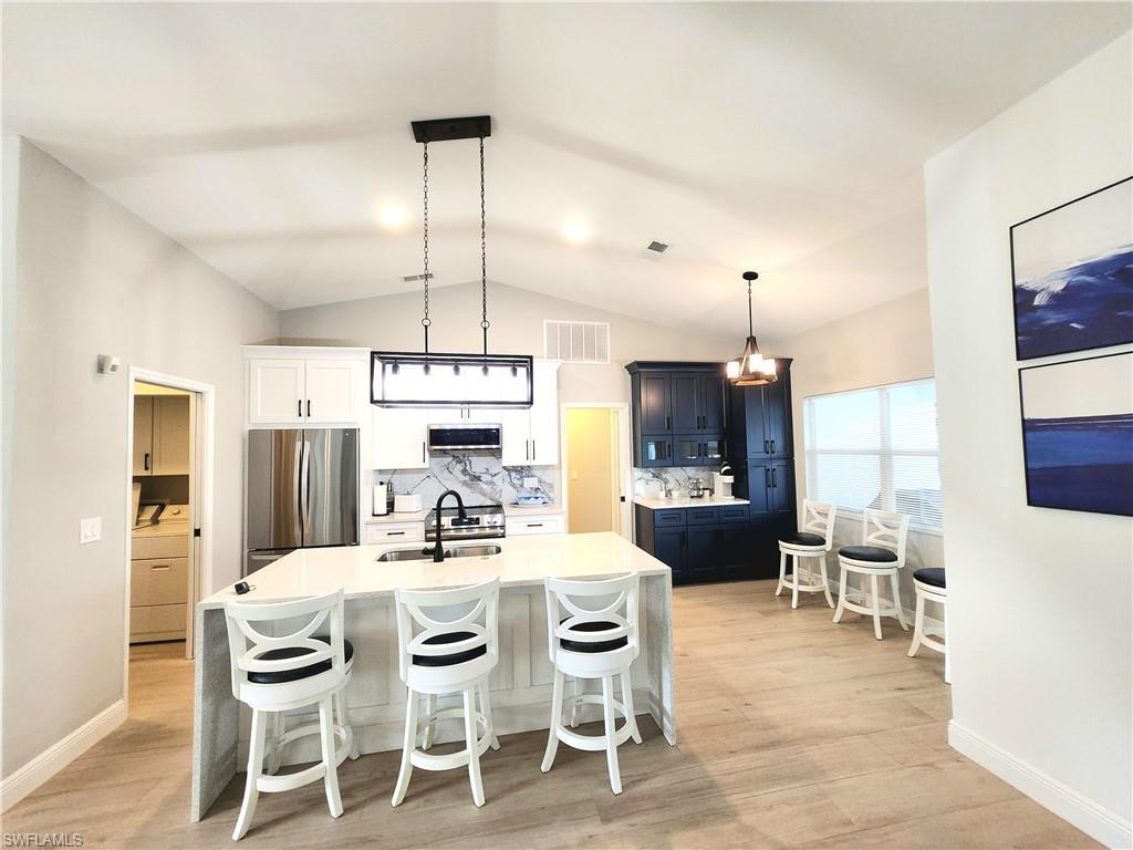 Image 1: Eat in Kitchen featuring pendant lighting with room for a table, lofted ceiling, appliances with stainless steel finishes, a breakfast bar area, and light hardwood / wood-style floors