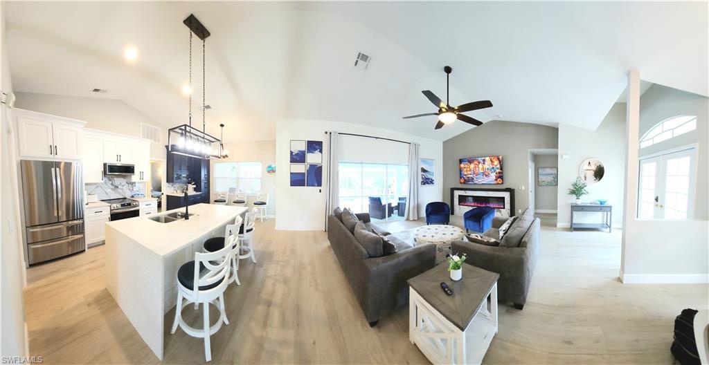 Image 4: Great open floor plan - Living room featuring light wood-type flooring, lofted ceiling, ceiling fan, and sink