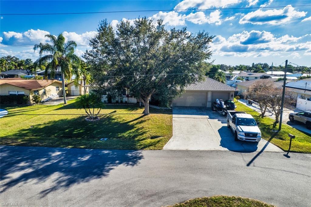 Image 4: View of property hidden behind natural elements with driveway, a residential view, a front lawn, and a garage