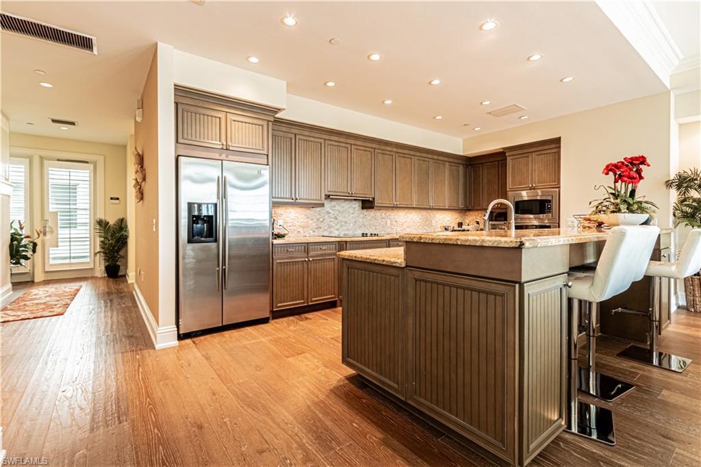 Image 3: Kitchen featuring light stone counters, light wood-style flooring, visible vents, appliances with stainless steel finishes, and decorative backsplash