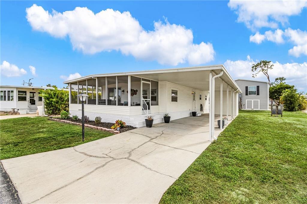Image 2: Manufactured / mobile home featuring a front yard, an attached carport, driveway, and a sunroom