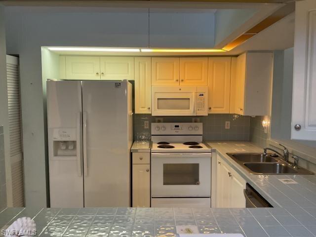 Image 2: Kitchen with tile counters, white appliances, tasteful backsplash, and white cabinetry