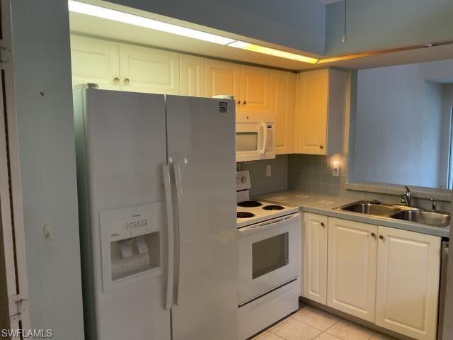 Image 3: Kitchen with white appliances, tasteful backsplash, light tile patterned floors, light countertops, and white cabinetry