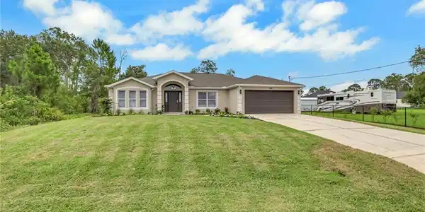 Image 2: Single-story residence featuring a stucco exterior with decorative trim, a two-car garage with a paneled door, and a concrete driveway