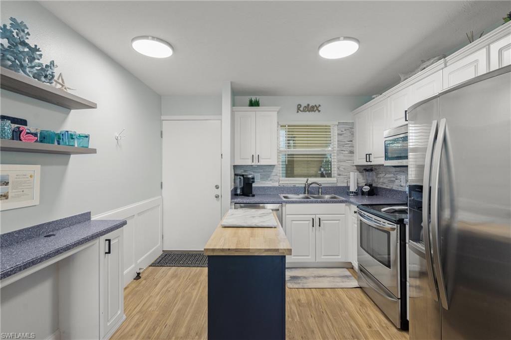 Image 3: Kitchen with wood counters, stainless steel appliances, light wood finished floors, white cabinetry, and a wainscoted wall