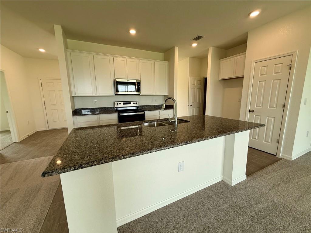 Image 2: Kitchen featuring dark colored carpet, white cabinets, recessed lighting, dark stone counters, and appliances with stainless steel finishes