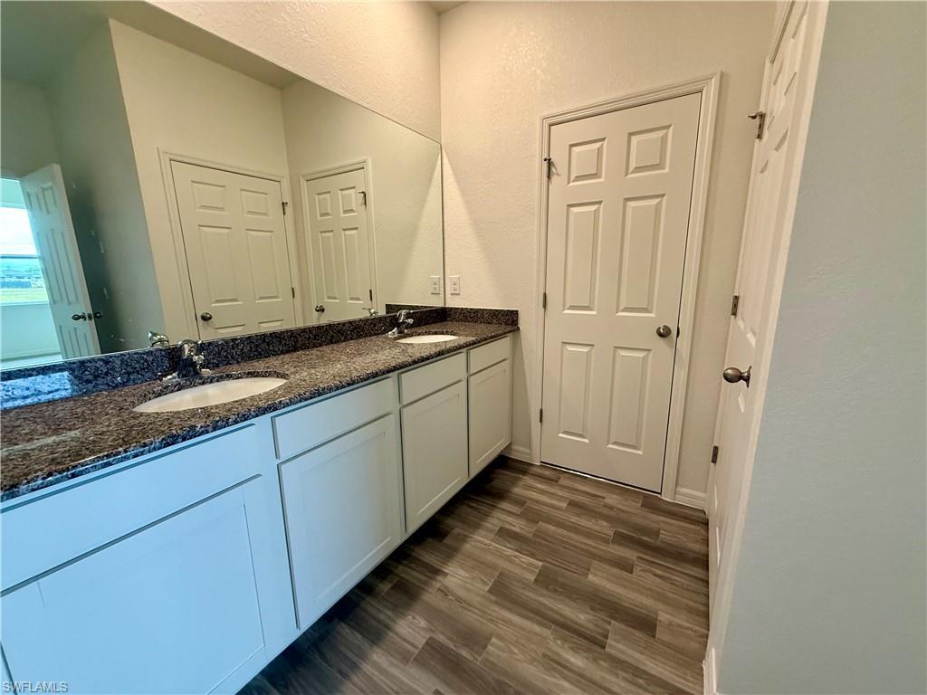 Image 4: Bathroom featuring double vanity, dark wood-style floors, and a textured wall