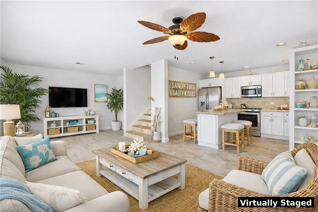 Image 1: Open-concept living space featuring wood-finish flooring, a contemporary kitchen with white cabinetry, stainless steel appliances, and a central island with bar seating