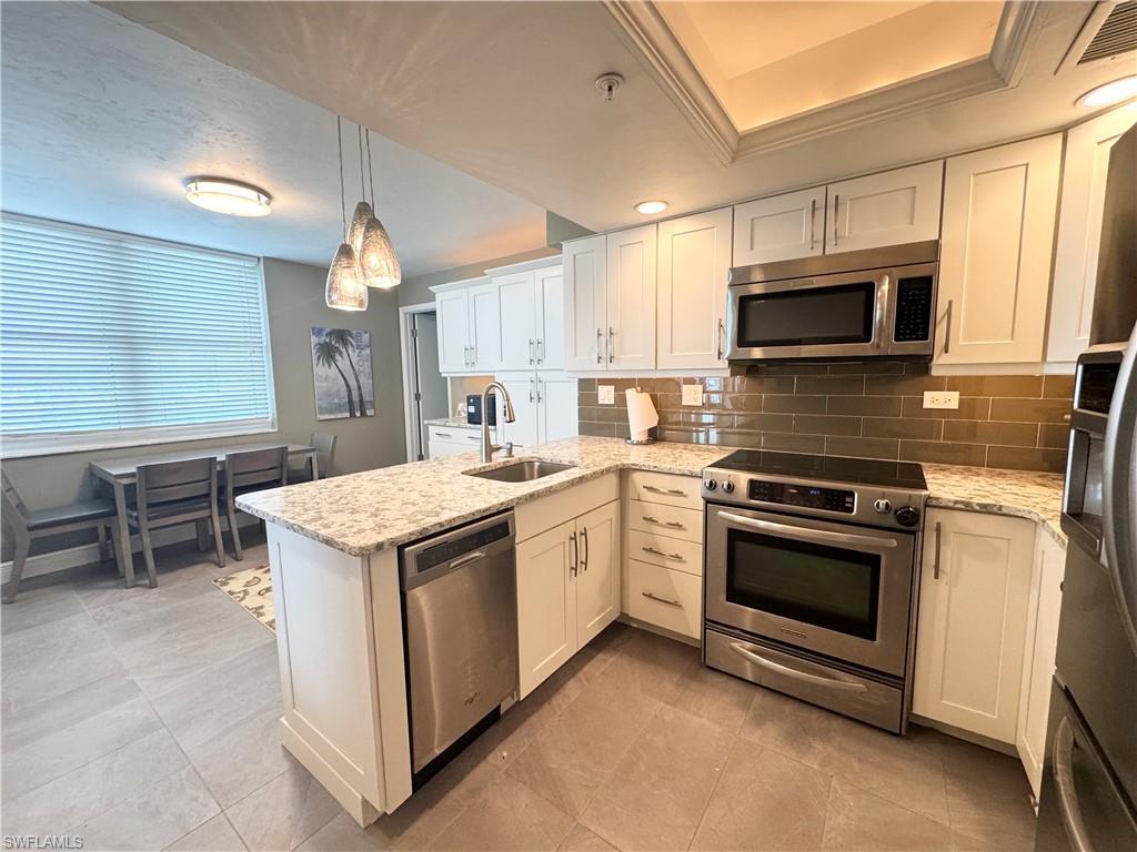 Image 4: Kitchen featuring appliances with stainless steel finishes, a peninsula, white cabinets, and decorative light fixtures
