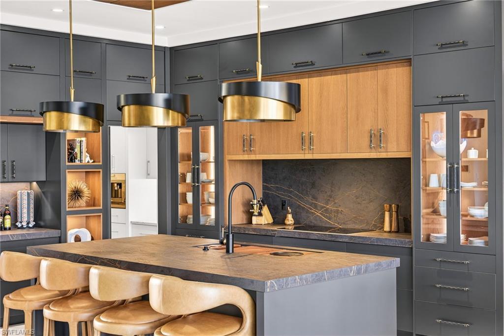 Image 1: Kitchen featuring two tone cabinets, decorative backsplash, a kitchen bar, and an island with sink