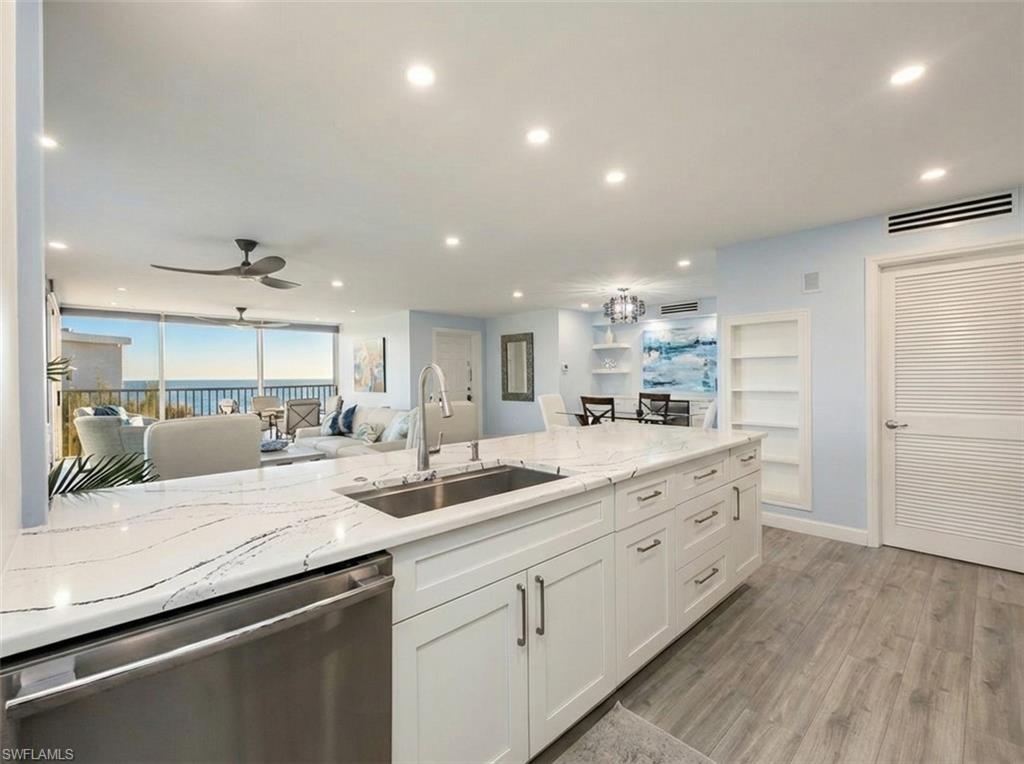 Image 2: Kitchen featuring stainless steel dishwasher, light stone counters, white cabinetry, light wood-style flooring, and open floor plan