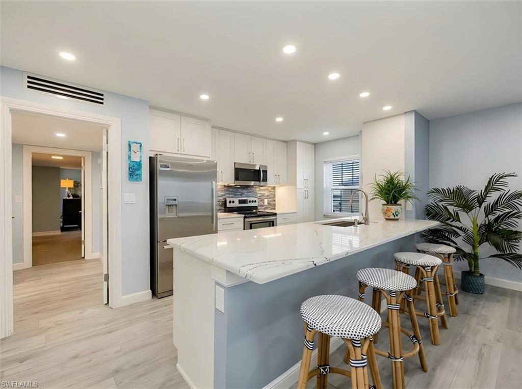 Image 3: Kitchen with stainless steel appliances, light stone counters, white cabinetry, light wood-style flooring, and a breakfast bar area