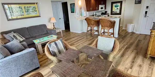 Image 3: Open-concept living space featuring wood-finish flooring, a contemporary ceiling fan, and a kitchen with rich wood cabinetry and a breakfast bar