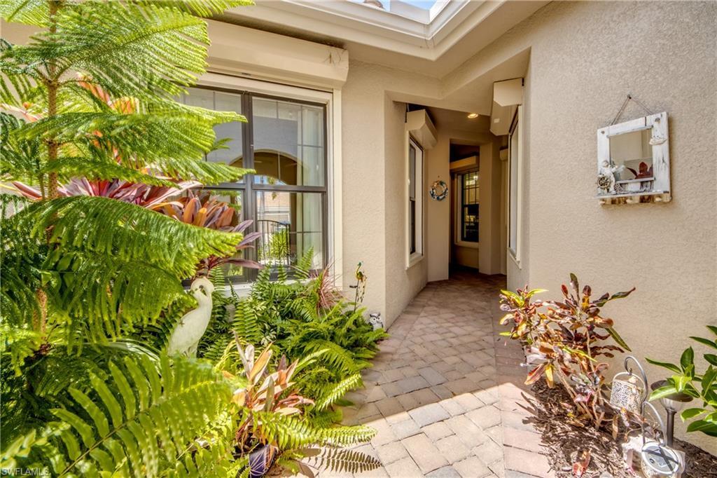 Image 4: Entryway featuring a paver stone walkway, stucco exterior, and lush tropical landscaping