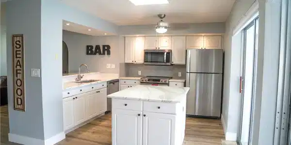 Image 3: Modern kitchen featuring white cabinetry, stainless steel appliances, and a central island with a stone countertop