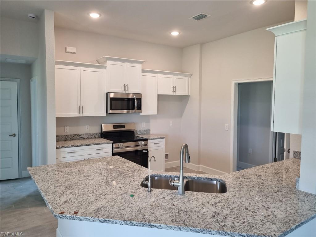 Image 4: Kitchen with stainless steel appliances, light stone counters, white cabinetry, recessed lighting, and a peninsula