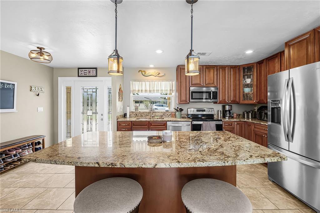 Image 4: Kitchen with stainless steel appliances, wood finish cabinetry, light stone countertops, glass fronted cabinets, and a kitchen bar