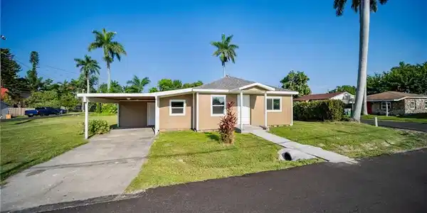Image 4: View of front facade with a front lawn, concrete driveway, and a carport