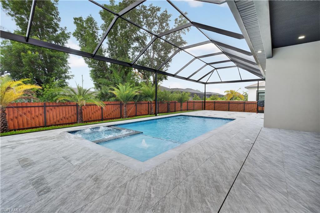 Image 2: Screened outdoor area featuring a swimming pool with integrated spa and water feature, light-toned patio tile, and a wooden privacy fence with mature palm trees
