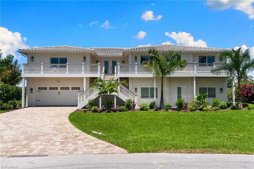 Image 1: Contemporary elevated residence featuring a two-car garage, upper-level balcony, dual exterior staircases, and a paver driveway