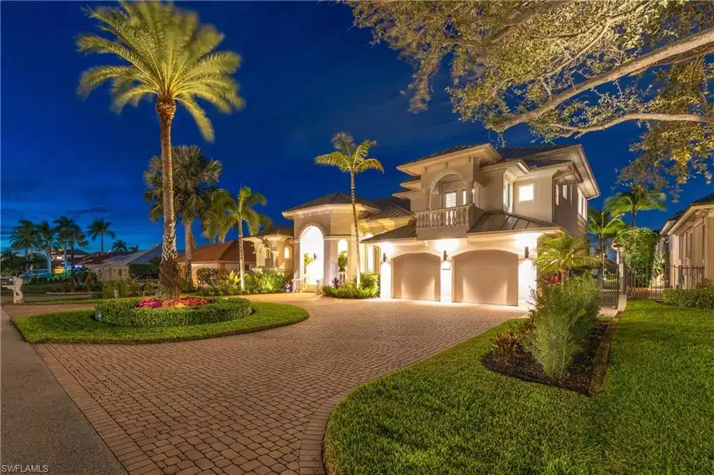 Image 1: The home has great curb appeal, with a large circular paver driveway, and is beautifully lit and landscaped