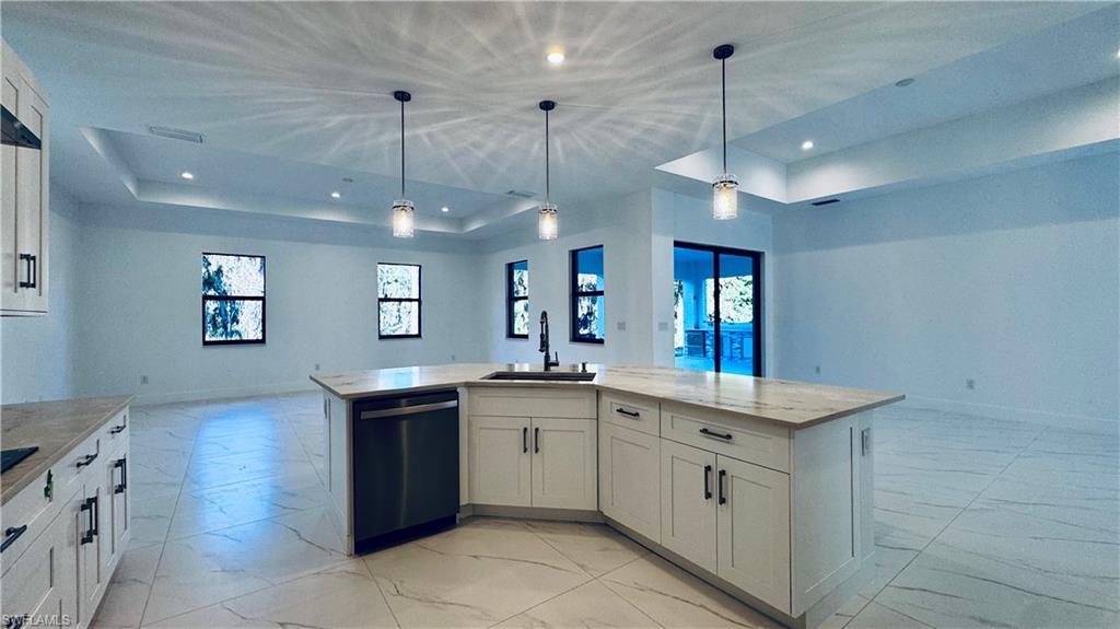 Image 4: Kitchen with open floor plan, white cabinets, an island with sink, stainless steel dishwasher, and light stone countertops