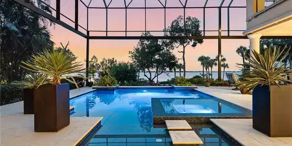 Image 2: After a day on the links, retreat to your private, custom-designed pool and spa and immerse yourself in the breathtaking beauty of Southwest Florida sunsets and abundant wildlife. Dramatic 35-foot picture-window screens creates an uninterrupted connection to the exquisitely landscaped beach and river beyond, allowing you to savor the views from the comfort of your private oasis. A truly exceptional private compound, designed for effortless relaxation, complete privacy, and refined waterfront living.