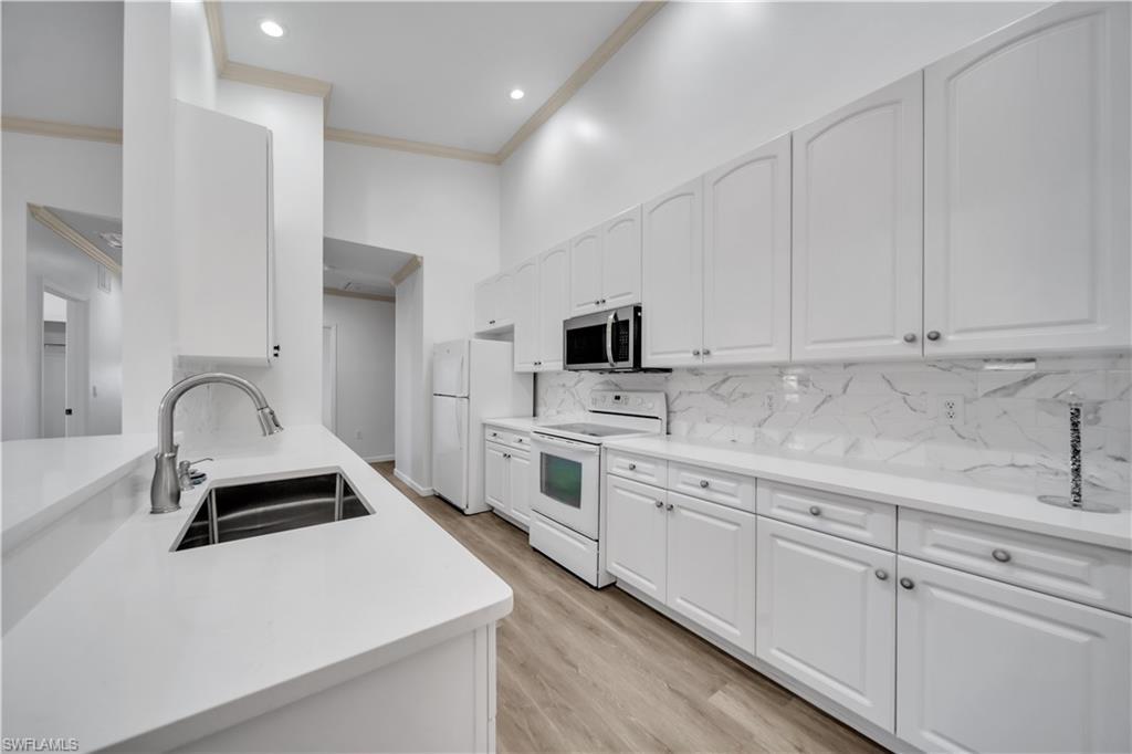 Image 1: Kitchen with white appliances, crown molding, white cabinetry, light wood-style floors, and light stone countertops