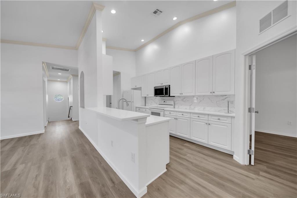 Image 3: Kitchen featuring a high ceiling, white cabinets, white appliances, light wood finished floors, and crown molding