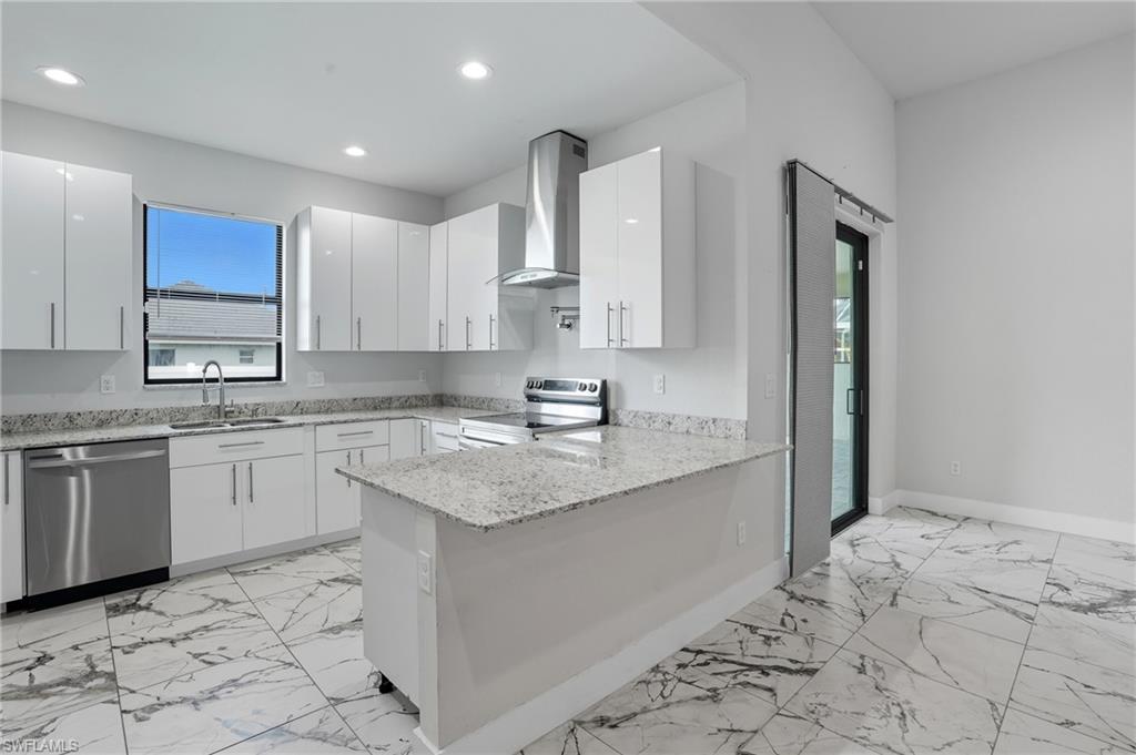 Image 2: Kitchen with light stone countertops, stainless steel appliances, wall chimney range hood, a peninsula, and white cabinets