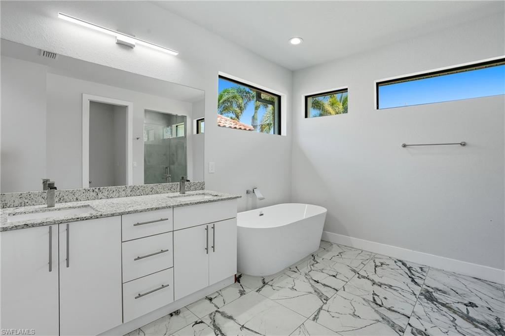 Image 3: Bathroom with double vanity, a stall shower, a soaking tub, light marble finish flooring, and recessed lighting