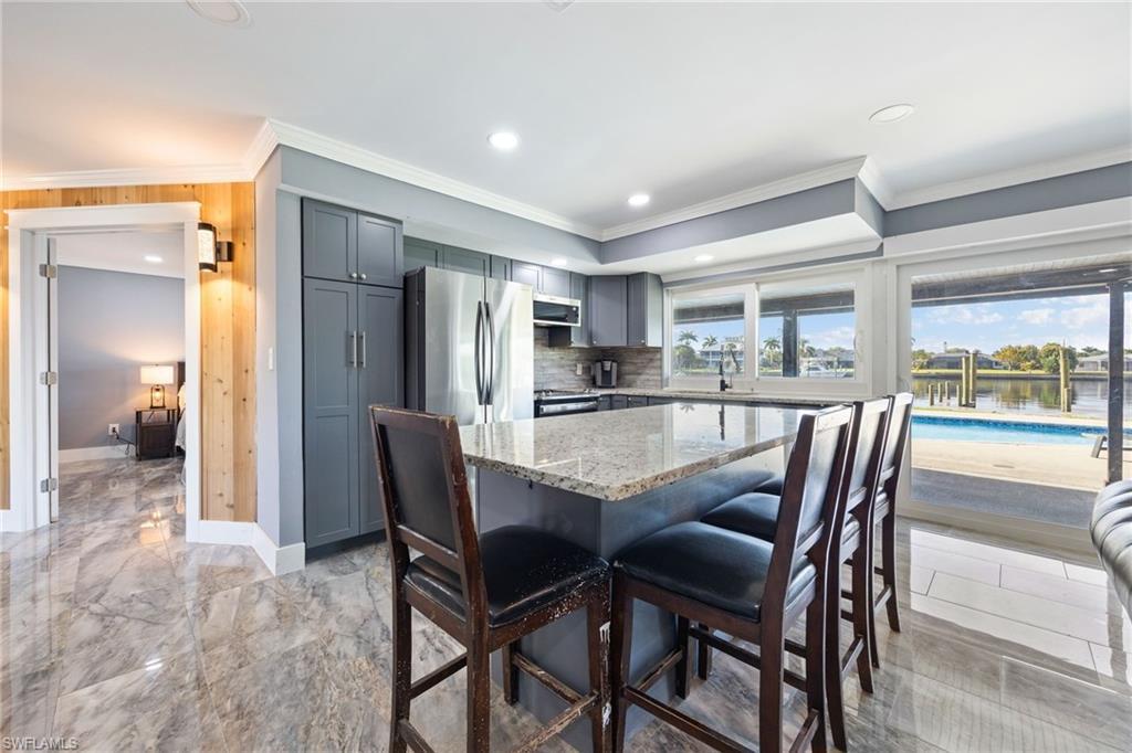 Image 2: Kitchen with gray cabinetry, stainless steel appliances, light stone counters, a center island, and a breakfast bar