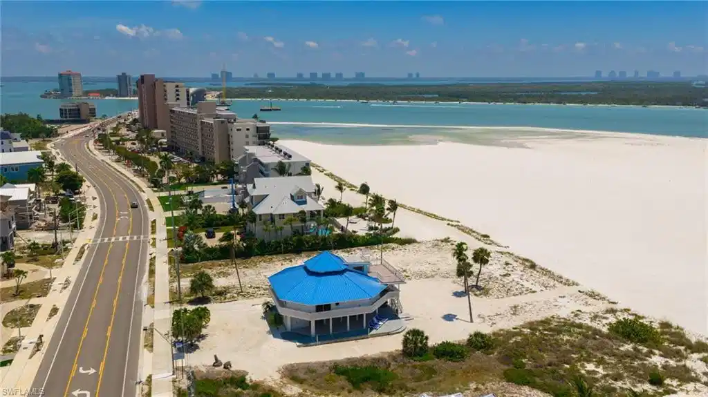 Image 1: Coastal property featuring a unique octagonal structure with a blue roof, white exterior, and elevated foundation - Virtually Edited Image