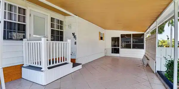 Image 3: Covered outdoor patio with large format tile flooring, a white railing, and exterior lighting