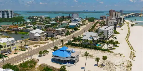 Image 3: Coastal property featuring a vibrant blue roof, multiple balconies, a raised foundation, and palm trees within a beach and canal-front environment - Virtually Edited Image