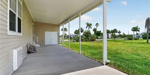 Image 3: Expansive covered patio with concrete flooring, supported by white posts, and featuring a light-toned vinyl siding exterior