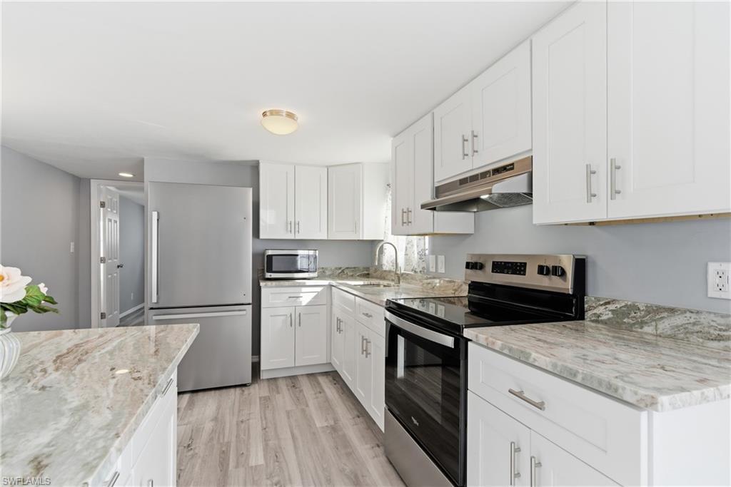 Image 4: Kitchen featuring stainless steel appliances, white cabinets, under cabinet range hood, and light wood finished floors